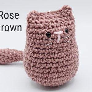 May include: A crocheted cat toy in rose brown with glitter yarn. The cat has black eyes and a pink nose with white whiskers.