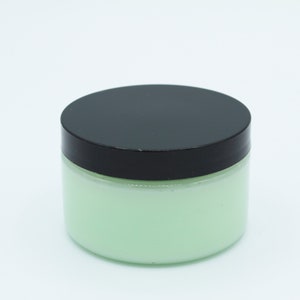 May include: A green jar with a black lid filled with a light green cream.