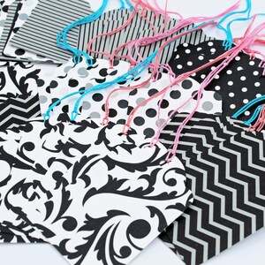Pode incluir: Um conjunto de etiquetas de presente com padrões em preto e branco com cordão rosa e azul amarrado. As etiquetas apresentam vários padrões, incluindo bolinhas, listras e um design de damasco.