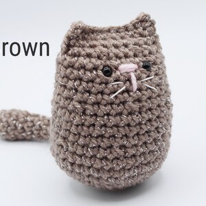 May include: A brown crocheted cat with black eyes and a pink nose. The cat has a sparkly finish.