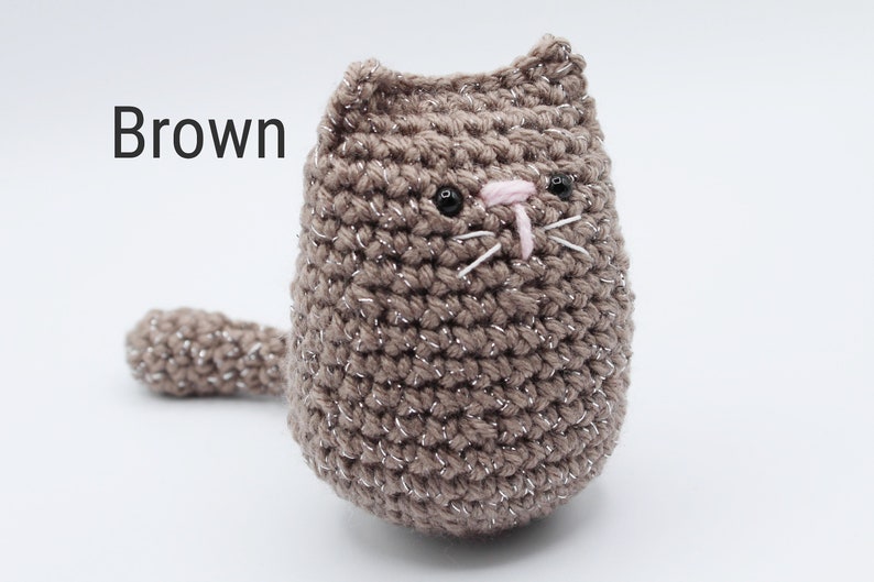 May include: A brown crocheted cat with black eyes and a pink nose. The cat has a sparkly finish.