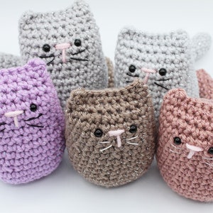 May include: Five crocheted cat toys in different colors, including purple, gray, brown, and pink. Each cat has black eyes, a pink nose, and black whiskers.