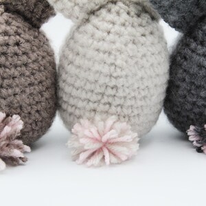 May include: Three crocheted stuffed animals with pink pom-pom tails. The animals are brown, gray, and dark gray.