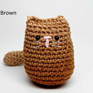 May include: A crocheted cat doll in shades of light brown. The handmade cat has black eyes, white whiskers, and a pink nose. The text "Light Brown" is in the upper left corner. The cat has a small tail.