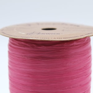 May include: A spool of pink paper ribbon with a brown label that reads "Berwick" and "A CSS Industries, Inc."