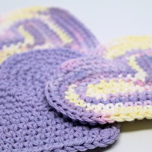 May include: Three crocheted heart-shaped dishcloths in shades of purple, pink, and yellow.