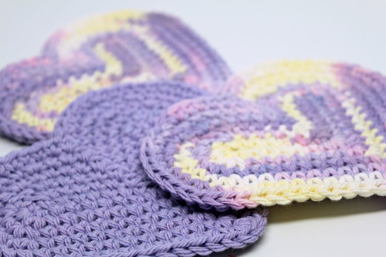 May include: Three crocheted heart-shaped dishcloths in shades of purple, pink, and yellow.