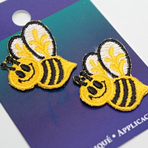 May include: Two yellow and black embroidered bee iron-on patches on a blue and purple card with the text "Wrights" and "Moqué - Aplicacion".