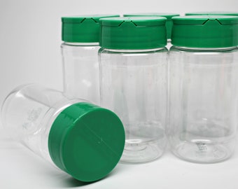 May include: Six clear glass spice jars with green lids. The jars are empty and have a textured surface.