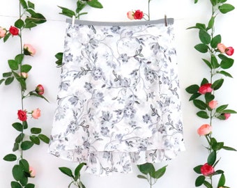 May include: A white skirt with a gray floral pattern. The skirt has a ruffled hem and is made of a lightweight fabric.