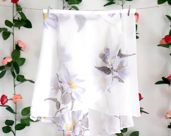 May include: A white chiffon dance skirt with a floral print. The skirt has a ruffled hem and is hanging on a clothesline.