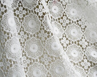 May include: White crochet fabric with a delicate floral pattern. The fabric is made of a fine, lightweight material and has a soft, airy feel.