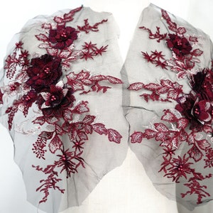 May include: Two burgundy floral appliques with pearl accents on a black mesh fabric. The appliques are ideal for adding a touch of elegance to any project.
