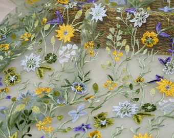 May include: Green sheer fabric with embroidered floral designs in yellow, blue, and white. The flowers are arranged in a repeating pattern.