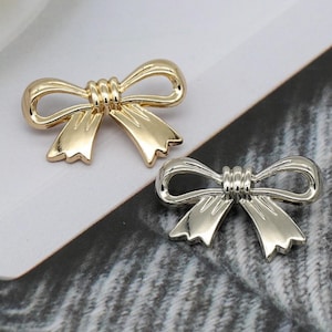 Könnte beinhalten: Zwei goldfarbene, bogenförmige Metallembellishments. Der Bogen links ist golden, der Bogen rechts ist silbern.