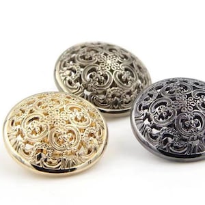 Puede incluir: Tres botones decorativos con un diseño intrincado y ornamentado. Los botones son dorados, plateados y negros.
