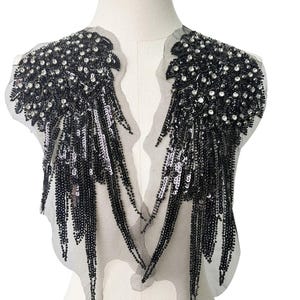 Peut inclure: Applique noire en perles et paillettes avec un design en V. L'applique présente un détail de frange et est parfaite pour ajouter une touche d'éclat aux vêtements ou aux accessoires.