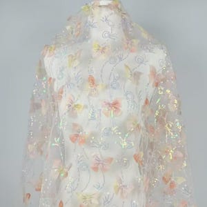 May include: White sheer fabric with iridescent sequins and 3D butterfly appliques in shades of pink, yellow, and orange.