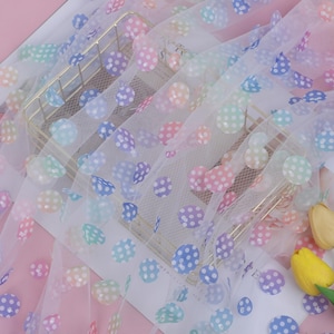 May include: White tulle fabric with a rainbow polka dot pattern. The dots are iridescent and have a subtle shimmer.