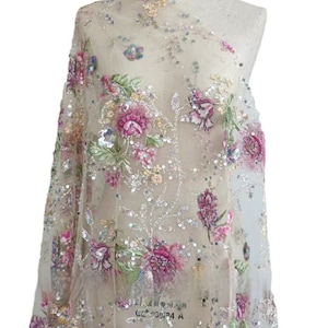 May include: Beige tulle fabric with floral embroidery and sequins. The flowers are pink, white, and green. The fabric has a delicate, feminine look.