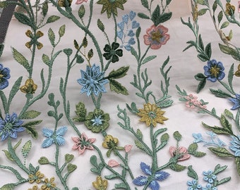 May include: A white sheer fabric with embroidered floral designs in shades of blue, green, pink, and yellow. The flowers are arranged in a random pattern and are connected by green stems.
