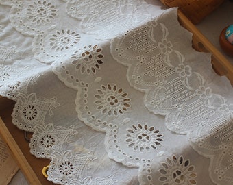 May include: White cotton lace trim with a scalloped edge and intricate eyelet designs. The lace has a delicate, feminine look and would be perfect for adding a touch of elegance to any project.