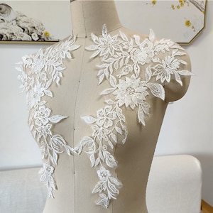 May include: White floral lace applique with delicate beading, ideal for adding a touch of elegance to wedding dresses, bridal accessories, or other craft projects.