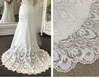 May include: A white lace wedding dress with a fitted bodice and a flowing skirt. The skirt features a delicate lace pattern and a scalloped hem.