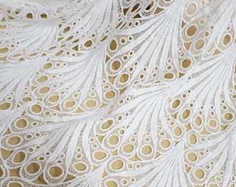 May include: White lace fabric with a delicate, intricate pattern of circles and leaves. The fabric has a soft, flowing texture and is perfect for creating elegant garments or home decor.