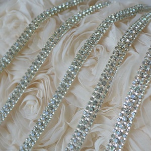 以下が含まれることがあります： 2列のラインストーンが付いたシルバーのラインストーントリムのクローズアップ。トリムは白い布の背景の上にあります。