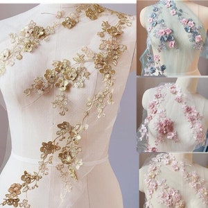 May include: Three different colours of floral lace trim with delicate flower designs. The lace is on a sheer mesh background. The colours are gold, light blue, and pink.