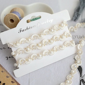 May include: White pearl and gold trim ribbon with the text "Fashion Jewelry" on a white card.