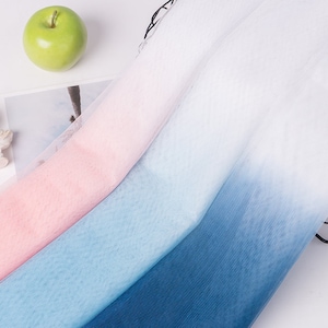 Puede incluir: Un primer plano de una tela de tul degradado en rosa, azul y blanco. La tela es suave y transparente, y es perfecta para manualidades y proyectos de bricolaje.