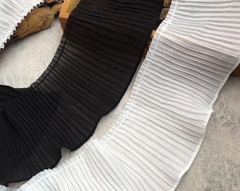 May include: Two pieces of pleated fabric trim, one black and one white. The trim is made of a soft, sheer material and has a delicate, ruffled edge.
