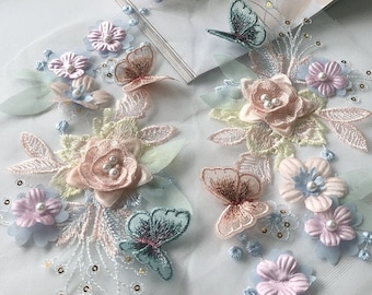 May include: A delicate floral embroidery design featuring pink, blue, and green flowers with butterflies. The embroidery is on a sheer white mesh fabric.