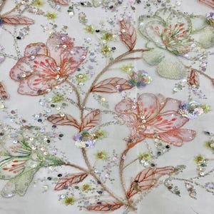 May include: A delicate floral embroidered fabric with pink and green flowers and leaves. The fabric is adorned with iridescent sequins.