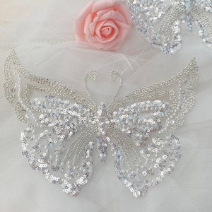 May include: A pair of silver sequined butterfly appliques. The butterflies are made of silver sequins and beads, and they have a delicate, feminine look.