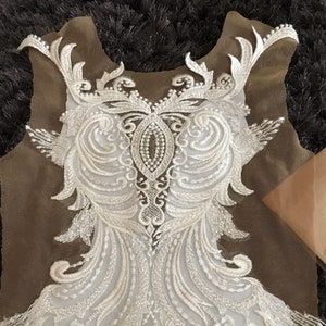 Peut inclure: Applique en dentelle blanche avec un motif floral délicat. La dentelle est fine et détaillée, avec un bord festonné. Cette applique serait parfaite pour ajouter une touche d'élégance à une robe de mariée, une robe de mariée ou une autre tenue de cérémonie.