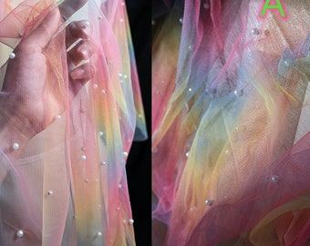 May include: Rainbow tulle fabric with white pearl embellishments. The fabric is sheer and has a soft, flowing texture.