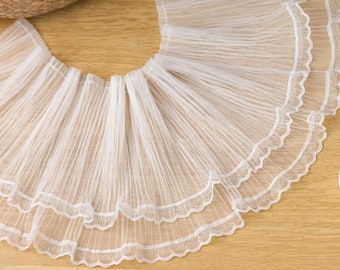 Puede incluir: Borde de encaje blanco con borde festoneado. El borde está plisado y tiene un aspecto delicado y femenino.