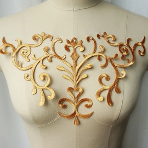 May include: Gold embroidered applique with a floral design. The applique is made of velvet and has a delicate, intricate pattern.