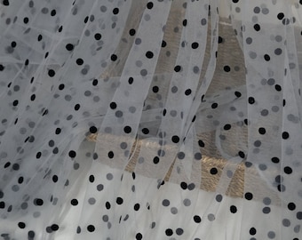 Peut inclure: Tissu de tulle blanc à pois noirs. Le tissu est transparent et a une texture douce et délicate.