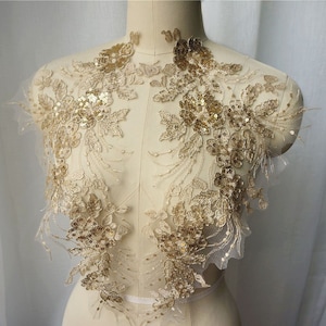 May include: Gold lace applique featuring sequins and floral designs. The applique is displayed on a white background and is ideal for adding a touch of elegance to any project.