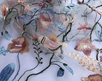 May include: A delicate floral embroidered tulle fabric with a light blue, pink, and yellow color scheme. The fabric is perfect for crafting, sewing, and creating unique projects.