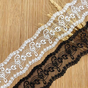 May include: Two decorative lace ribbons, one white and one black, with a musical note pattern. The white ribbon has a floral border, and the black ribbon has a scalloped edge. The ribbons are shown against a natural, textured background.