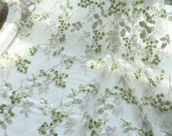 Könnte beinhalten: Ein transparenter weißer Tüllstoff mit einem komplizierten Stickmuster aus zarten Zweigen mit Blättern und kleinen Beerenclustern. Das Design ist mit schimmernden hellgrünen und silbernen Pailletten verziert, die das Licht reflektieren.