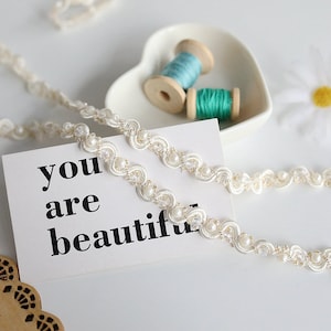 May include: White beaded trim with a scalloped edge and a message card that reads "you are beautiful".