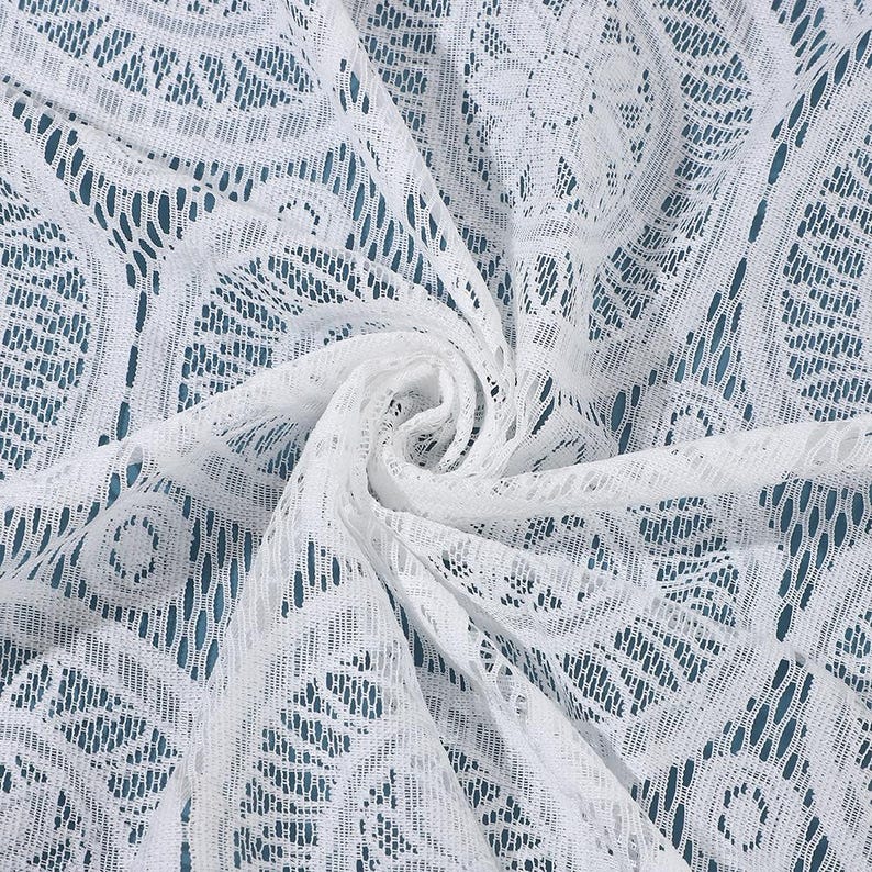 Peut inclure: Un tissu en dentelle blanche pr&eacute;sentant un motif floral et g&eacute;om&eacute;trique r&eacute;p&eacute;titif avec un design en maille ajour&eacute;e. Le mat&eacute;riau est rassembl&eacute; au centre, cr&eacute;ant un effet tourbillonnant qui met en valeur la texture complexe et le tissage d&eacute;licat.