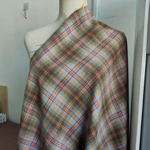 May include: A swatch of plaid fabric draped over a mannequin. The fabric features a brown, blue, orange, and green plaid pattern. The fabric is likely wool or a wool blend, suitable for clothing or home decor.