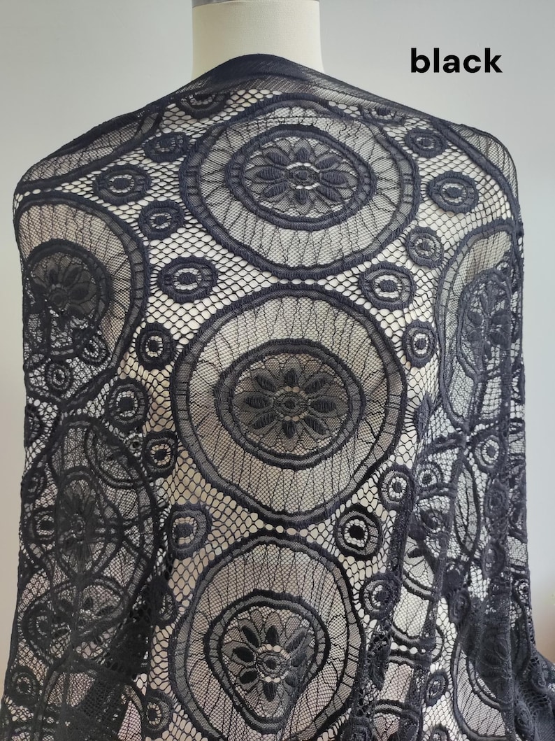 Peut inclure: Un tissu en dentelle noire pr&eacute;sentant un motif r&eacute;p&eacute;titif de grands m&eacute;daillons circulaires avec des centres floraux complexes, reli&eacute;s par un filet fin. Le mot black est imprim&eacute; dans le coin sup&eacute;rieur droit de l'image.